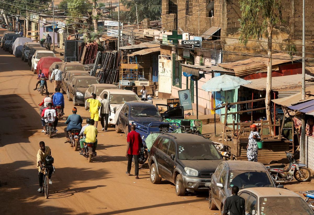 Mali'de yakıt kıtlığı: Bisikletli ve motosikletli kişiler araçların yanından geçiyor.